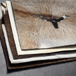 May include: A stack of cowhide rugs with a black and white cowhide design on the top rug.