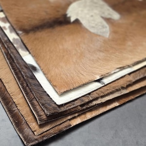 May include: A stack of brown, white, and black cowhide rugs with a natural, textured surface.