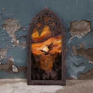 Könnte beinhalten: Ein gotischer Wandbehang in Bogenform mit einem dunklen, strukturierten Rahmen und filigranen Vierpass-Details an der Spitze. Das zentrale Kunstwerk zeigt die Silhouette eines fliegenden Drachen vor einem leuchtend orange-gelben Sonnenuntergang.