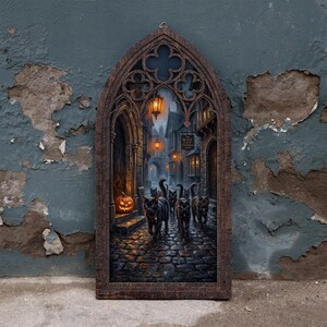 May include: A gothic arched wall hanging featuring a dark cobblestone street scene with several black cats, glowing lanterns, and a lit jack-o'-lantern. A sign on the building reads The Black Cats Tavern. The frame has an ornate, carved wood appearance.
