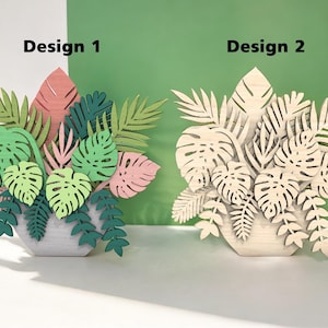 Puede incluir: Dos diseños de plantas de madera, uno con hojas verdes y rosas y el otro con hojas de madera natural. Ambos diseños están en una maceta blanca y están etiquetados como "Diseño 1" y "Diseño 2".