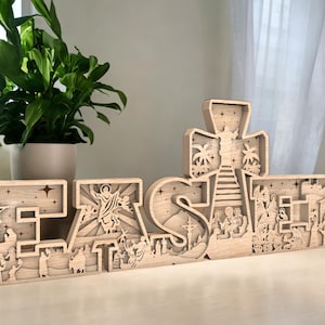 Puede incluir: Un letrero de Pascua de madera con la palabra "Pascua" escrita en letras individuales. Cada letra está tallada con intrincados detalles de escenas bíblicas, incluyendo la cruz, la natividad y la resurrección.