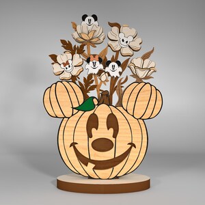 Puede incluir: Una calabaza de madera con cara y orejas de Mickey Mouse, decorada con flores blancas y pequeñas figuras de Mickey Mouse.