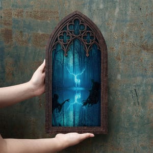 May include: A dark brown wooden frame with a pointed gothic arch top containing a print of a glowing white stag standing in a dark blue forest. The image features a reflection of the stag in water and two dark, shadowy figures on either side.