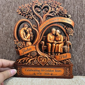 Könnte beinhalten: Eine dekorative Holztafel mit einem geschnitzten Baum und Rosen, die ein junges Paar links und ein älteres Paar auf einer Bank rechts zeigt. Sie enthält den Text "Rooted in Love, Growing in Life, Together Forever," "John," "Pat," "50," und "Celebrating 50 Golden Years 1976 - 2026."