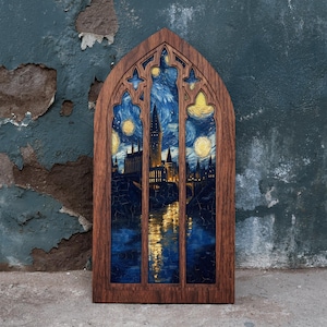 Puede incluir: Un marco de madera en arco apuntado que contiene una impresión de la silueta de un castillo contra un cielo nocturno azul oscuro con estrellas amarillas brillantes y el reflejo de luces doradas en el agua, imitando un vitral.