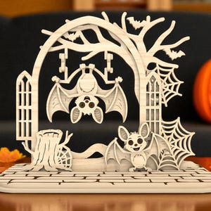Könnte beinhalten: Eine hölzerne Halloween-Dekoration mit Fledermäusen, einem Baum, einem Spinnennetz und einem Kürbis. Die Fledermäuse hängen am Baum und die Dekoration steht auf einer ziegelartigen Basis. Die Dekoration ist aus hellem Holz gefertigt.