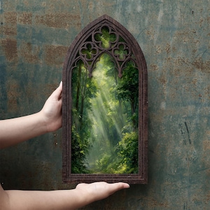May include: A dark brown wooden frame shaped like a pointed gothic arch with decorative quatrefoil cutouts at the top. The frame contains a printed image of a lush green forest with sunlight streaming through the trees and dense foliage.