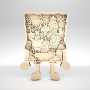 Op de afbeelding: Houten lasergesneden kunstwerk met SpongeBob SquarePants, Patrick Star en Octo Tentakel, met SpongeBobs ananas huis op de achtergrond. Het kunstwerk heeft een gelaagd ontwerp met een lichte houten afwerking.