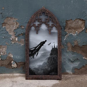May include: A dark brown, arched wooden frame with gothic-style tracery at the top, enclosing a black and white print. The image depicts a silhouetted figure with flowing, tattered robes flying toward a large castle perched on a rocky mountain cliff.
