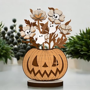 May include: Wooden Halloween decoration featuring a carved pumpkin with a jack-o'-lantern face. The pumpkin holds a bouquet of wooden flowers, some with skull designs, and small ghost figures. The decoration is on a round wooden base.