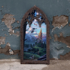 Könnte beinhalten: Ein dunkelbrauner Holzrahmen mit spitzem gotischem Bogen, der eine Fantasy-Illustration eines hohen Schlosses auf einem Hügel, zwei fliegende Drachen und eine Person auf einem weißen Pferd auf einem Pfad durch eine grüne Landschaft zeigt.