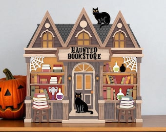 Puede incluir: Modelo de madera de una librería encantada con una calabaza. El modelo presenta un letrero que dice "HAUNTED BOOKSTORE", un gato negro en el tejado y un gato negro en el porche. Las estanterías están llenas de libros y decoraciones de Halloween.