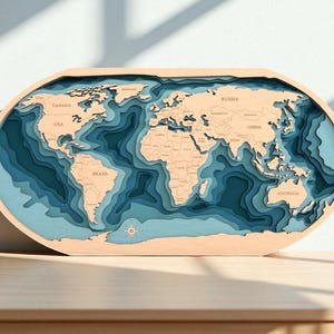 May include: A layered wooden world map, featuring continents in light brown and oceans in varying shades of blue. The oval-shaped map displays country names and is set on a wooden surface.