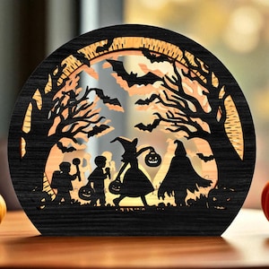 May include: A round, black wooden Halloween decoration with a silhouette design. The design features a witch, children trick-or-treating, bats, and trees. The background is illuminated with a warm, orange glow, creating a festive ambiance.