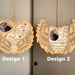 Könnte beinhalten: Zwei herzförmige Holzornamente mit Engelsflügeln. Das erste Ornament zeigt ein Unendlichkeitszeichen mit einem Fotoplatz und dem Text "Ich habe einen Engel, der über mich wacht, ich nenne ihn Papa". Das zweite Ornament zeigt einen Fotoplatz und den Text "Mein Vater ist mein Schutzengel, er wacht über mich".