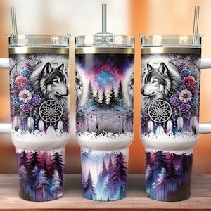 Pode incluir: Três copos de aço inoxidável com fundo branco e um design colorido que apresenta um lobo, flores e um apanhador de sonhos. Os copos têm uma alça e uma tampa com um canudo.