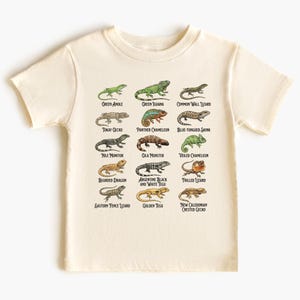 Könnte beinhalten: Cremefarbenes T-Shirt mit einer farbenfrohen, illustrierten Tabelle verschiedener Echsenarten, darunter der Grüne Leguan, der Bartagame und der Goldteju. Das Shirt hat kurze Ärmel und einen Rundhalsausschnitt.