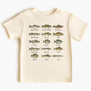 May include: A cream-coloured t-shirt displaying detailed illustrations of various fish species, such as Rainbow Trout and Smallmouth Bass, each labelled with its name. The design has an educational style. The t-shirt is made of a soft material.