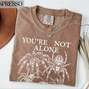 Brown t-shirt with "YOU'RE NOT ALONE" and spider graphic.