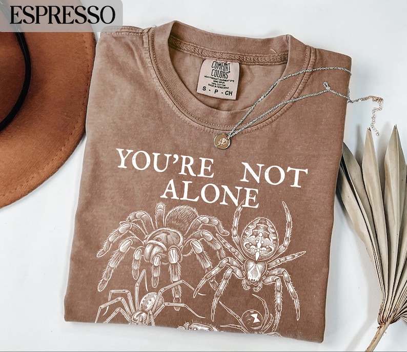 Brown t-shirt with "YOU'RE NOT ALONE" and spider graphic.