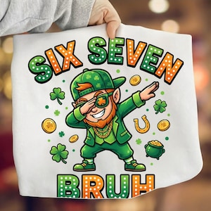 Puede incluir: Bolso tote blanco con un duende de dibujos animados haciendo dab, vestido de verde y con gafas de sol. El bolso muestra el texto "SIX SEVEN BRUH" en verde y naranja. También se representan monedas de oro, una herradura y tréboles.
