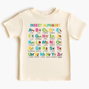 May include: Cream-colored t-shirt featuring a colorful insect alphabet design. Each letter is paired with an insect illustration and its name, from Ant to Zebra butterfly. The shirt is a fun educational tool for children.