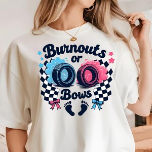K&ouml;nnte beinhalten: Wei&szlig;es T-Shirt mit einem Grafikdesign aus zwei Reifenspuren, eine blaue und eine rosa, mit dem Text "Burnouts or Bows" und einem Paar Baby-Fu&szlig;abdr&uuml;cken.