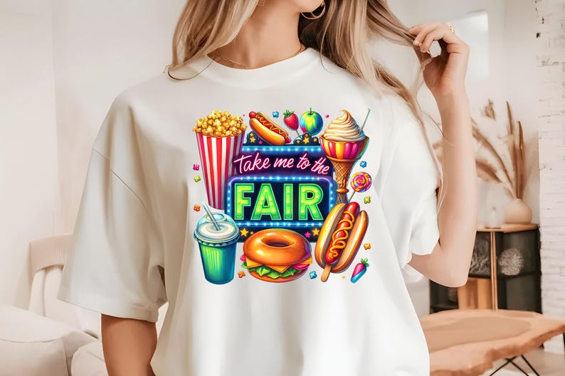 May include: White t-shirt with a colorful graphic design featuring fair food like popcorn, hot dogs, ice cream, and a donut. The graphic also includes a neon sign that says "Take me to the Fair".