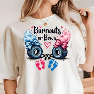 K&ouml;nnte beinhalten: Wei&szlig;es T-Shirt mit einem Aufdruck von zwei Baby-Fu&szlig;abdr&uuml;cken, einem rosa und einem blauen. Der Aufdruck enth&auml;lt auch zwei Reifen mit Schleifen, einen blauen und einen rosa, sowie den Text "Burnouts or Bows".