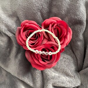 Könnte beinhalten: Ein hellgrünes Perlenarmband mit rosa Herzperlen und den Buchstaben "LN4" in Schwarz.