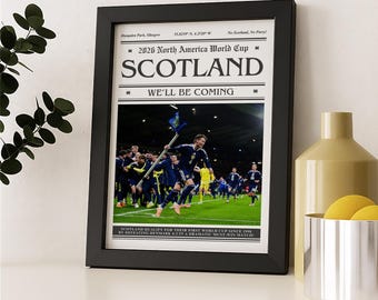 May include: Framed print featuring a soccer team celebrating on a green field. The print has the text "2026 North America World Cup SCOTLAND WE'LL BE COMING". The frame is black and the print is displayed on a white surface.