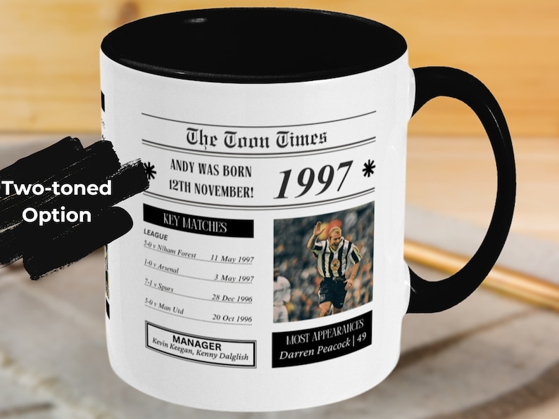 May include: A black and white mug with a newspaper design featuring the text "The Toon Times" and "1997". The mug has a black handle and a black rim.