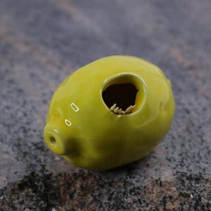 Pode incluir: Um pequeno cofrinho de cerâmica amarelo com um buraco no topo para moedas. O cofrinho tem a forma de um porco e tem um acabamento esmaltado.