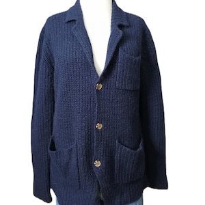 Puede incluir: Un cárdigan de punto azul marino con cierre de botones y dos bolsillos de parche. El cárdigan tiene un corte holgado y un punto ligeramente texturizado.