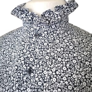 May include: A black and white floral print shirt with a ruffled collar. The collar is a stand-up style and has a button closure.