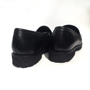 May include: Pair of black leather loafers with a thick, black sole. The shoes are shown from a low angle, highlighting the shape and texture of the leather. The loafers have a classic, slip-on design, suitable for various occasions.