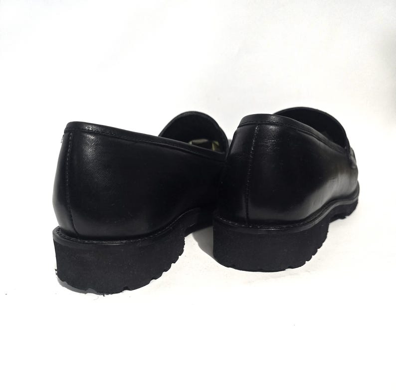 May include: Pair of black leather loafers with a thick, black sole. The shoes are shown from a low angle, highlighting the shape and texture of the leather. The loafers have a classic, slip-on design, suitable for various occasions.