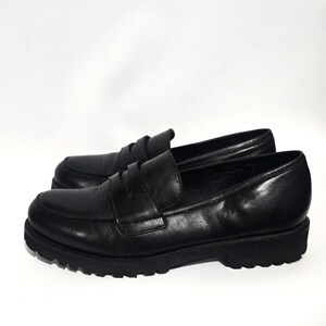 May include: A pair of black leather penny loafers. The shoes have a classic design with a rounded toe, a strap across the vamp, and a chunky, lugged sole. The leather appears smooth and polished.