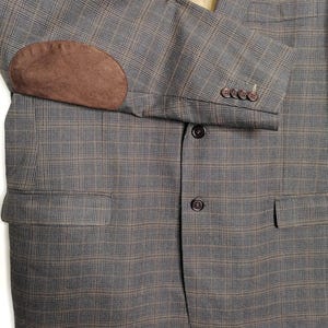 Puede incluir: Una chaqueta de traje de cuadros marrones y grises con un parche de ante marrón en el codo y botones marrones.