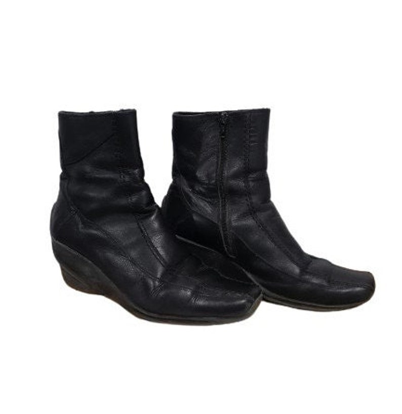 May include: A pair of black leather ankle boots with a wedge heel. The boots have a zip on the inside of each boot.
