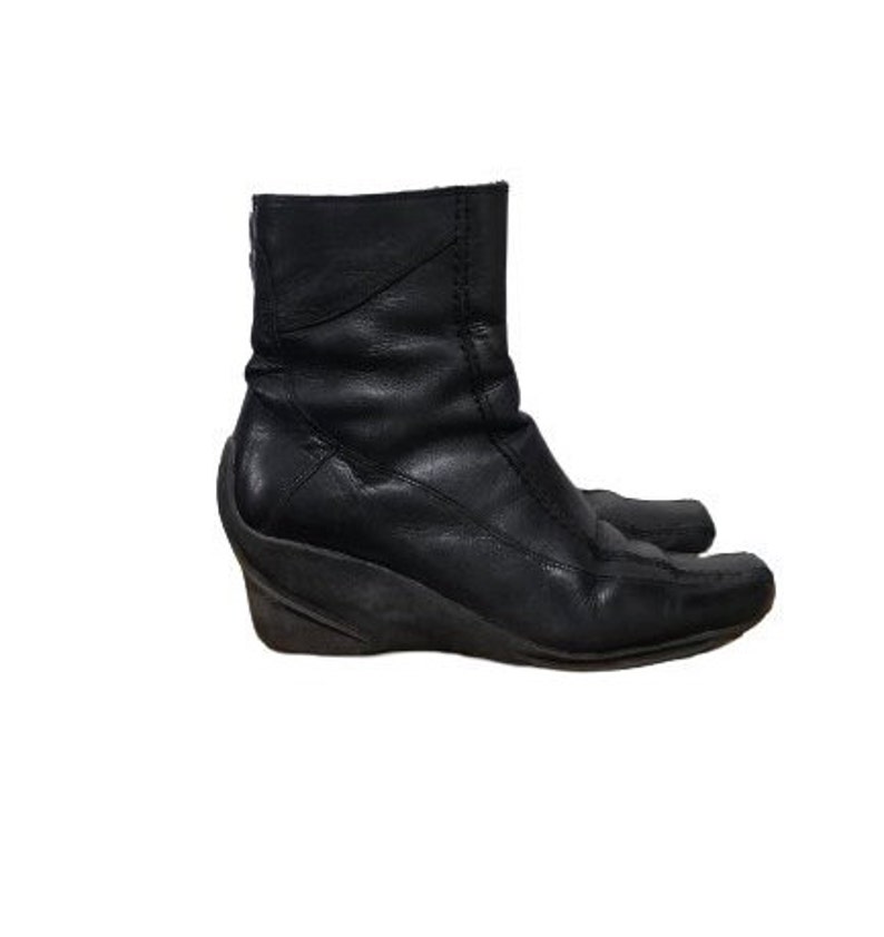 May include: Black leather ankle boots with a wedge heel. The boots have a pointed toe and a zip on the inside of the ankle.