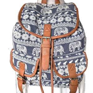 Peut inclure: Un sac à dos en toile bleu avec un imprimé d'éléphants blancs et des accents en cuir marron. Le sac à dos a deux poches avant et une fermeture à cordon.