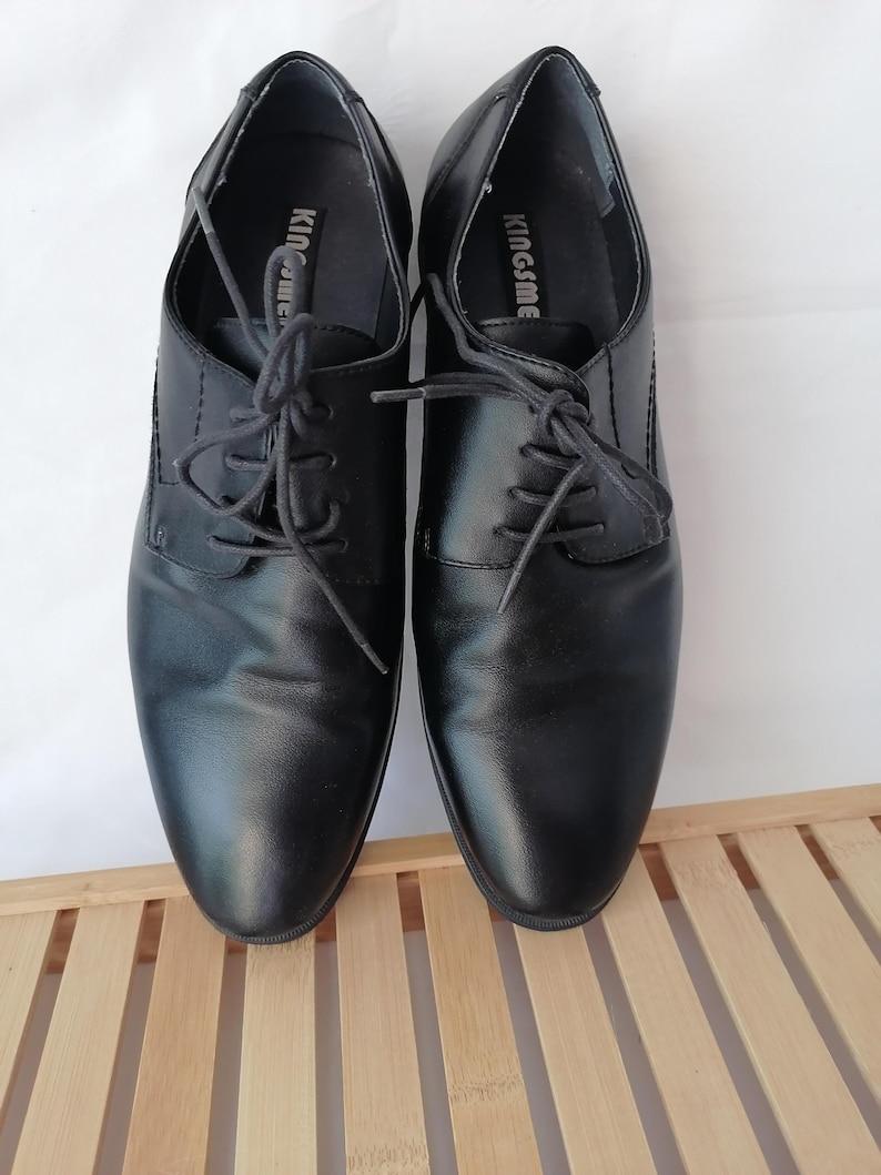 May include: A pair of black leather lace-up shoes with the brand name "Kingsme" printed on the inside of each shoe.