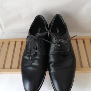 May include: A pair of black leather lace-up shoes with the word "KING" printed on the inside of each shoe.