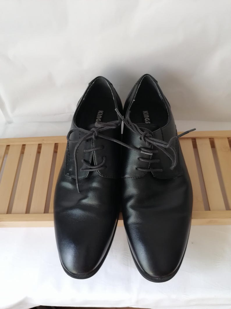 May include: A pair of black leather lace-up shoes with the word "KING" printed on the inside of each shoe.