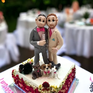 May include: A wedding cake topper featuring two grooms in grey and beige suits, holding hands. The cake is decorated with red and white flowers and three small dog figurines.