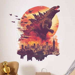 Op de afbeelding: Een Godzilla-monstersilhouet met een rode en oranje zonsondergangachtergrond, een stadsbeeld en straaljagers die eroverheen vliegen. Het monster staat op een stad met hoge gebouwen.