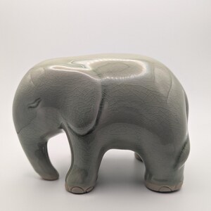 May include: A grey ceramic elephant ornament. The elephant has a textured, crackled finish and is standing on four short legs. The trunk is small and the ears are rounded. A decorative item for the home.