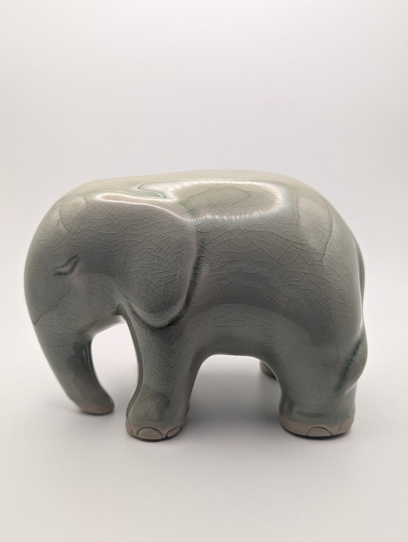 May include: A grey ceramic elephant ornament. The elephant has a textured, crackled finish and is standing on four short legs. The trunk is small and the ears are rounded. A decorative item for the home.